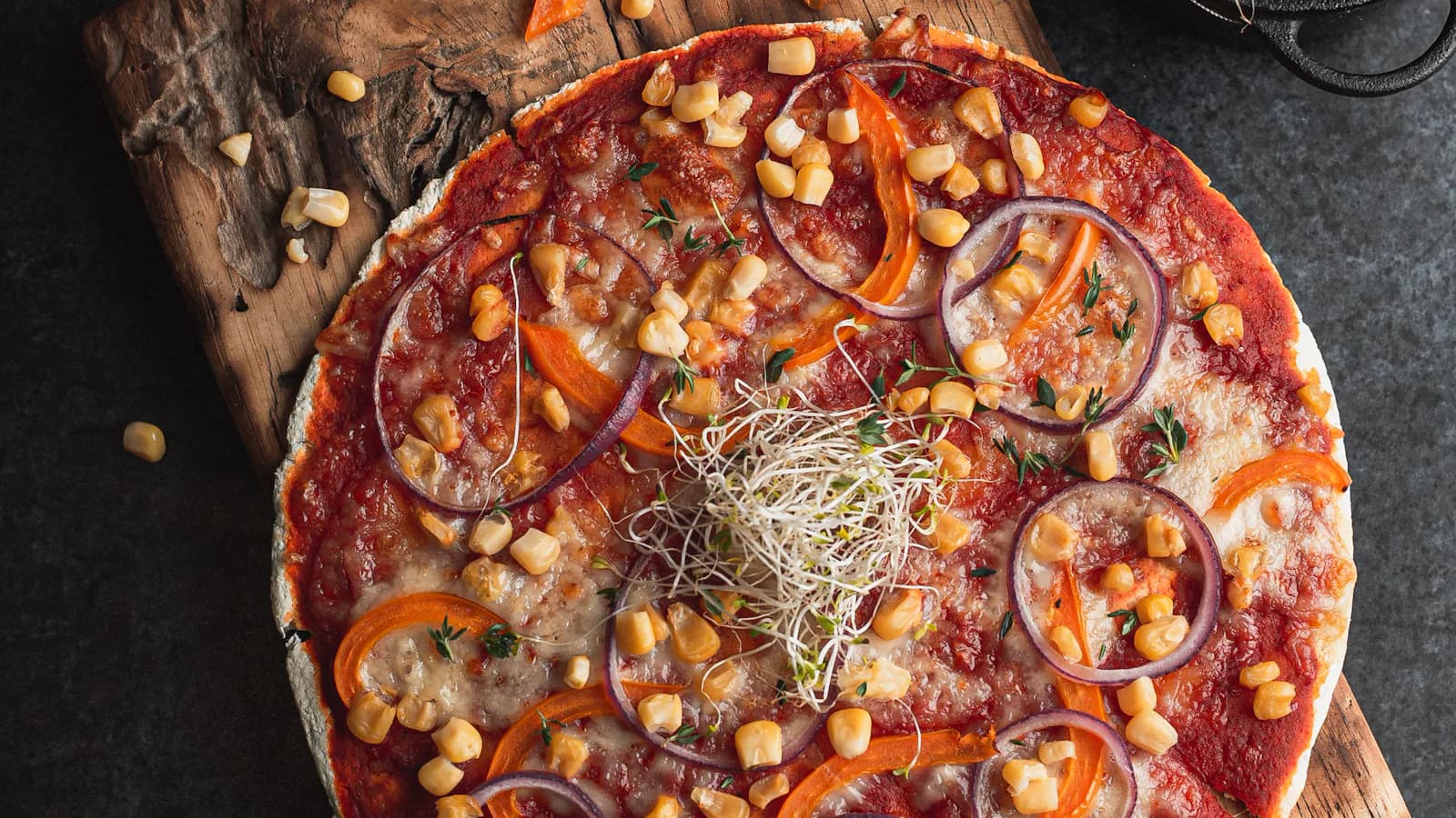 Pizza avec maïs, oignon et pousses sur une planche en bois