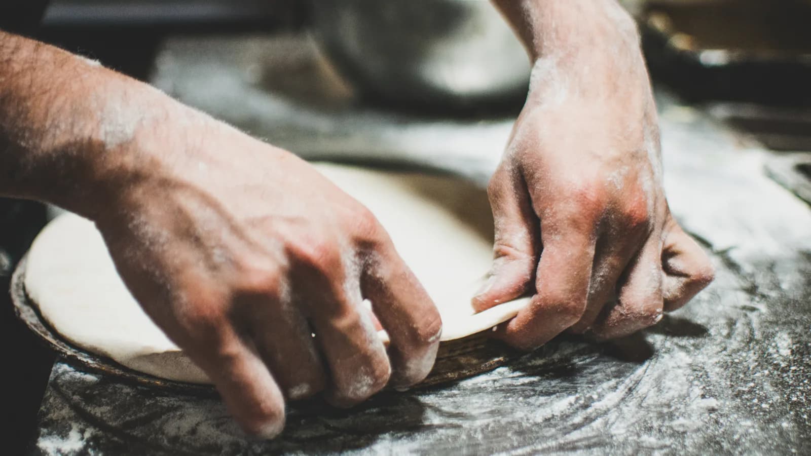 Personne qui pétrit la pâte à pizza sur une table - matière première