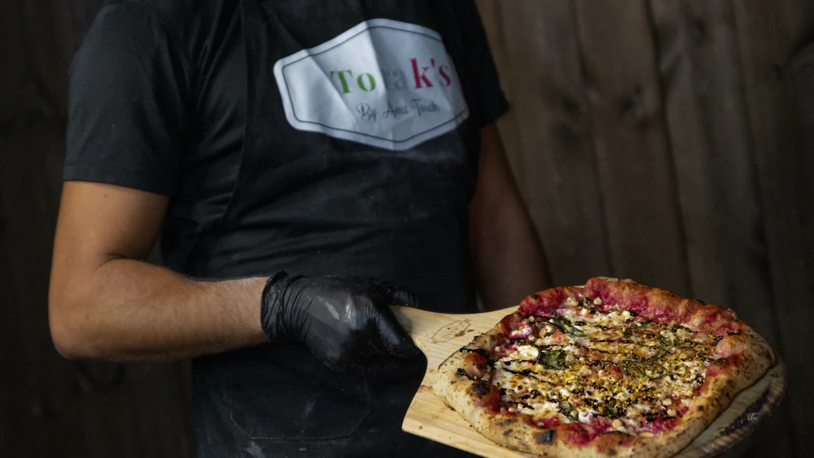 Pizzaiolo qui présente une pizza fraîche sur une pelle en bois