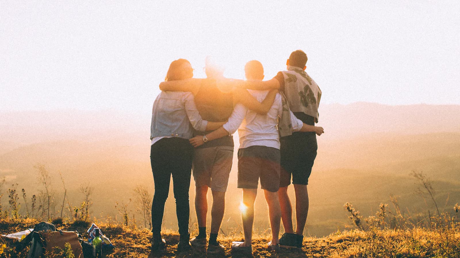 Quatre personnes bras autour des épaules face au coucher de soleil - amis, parrainage