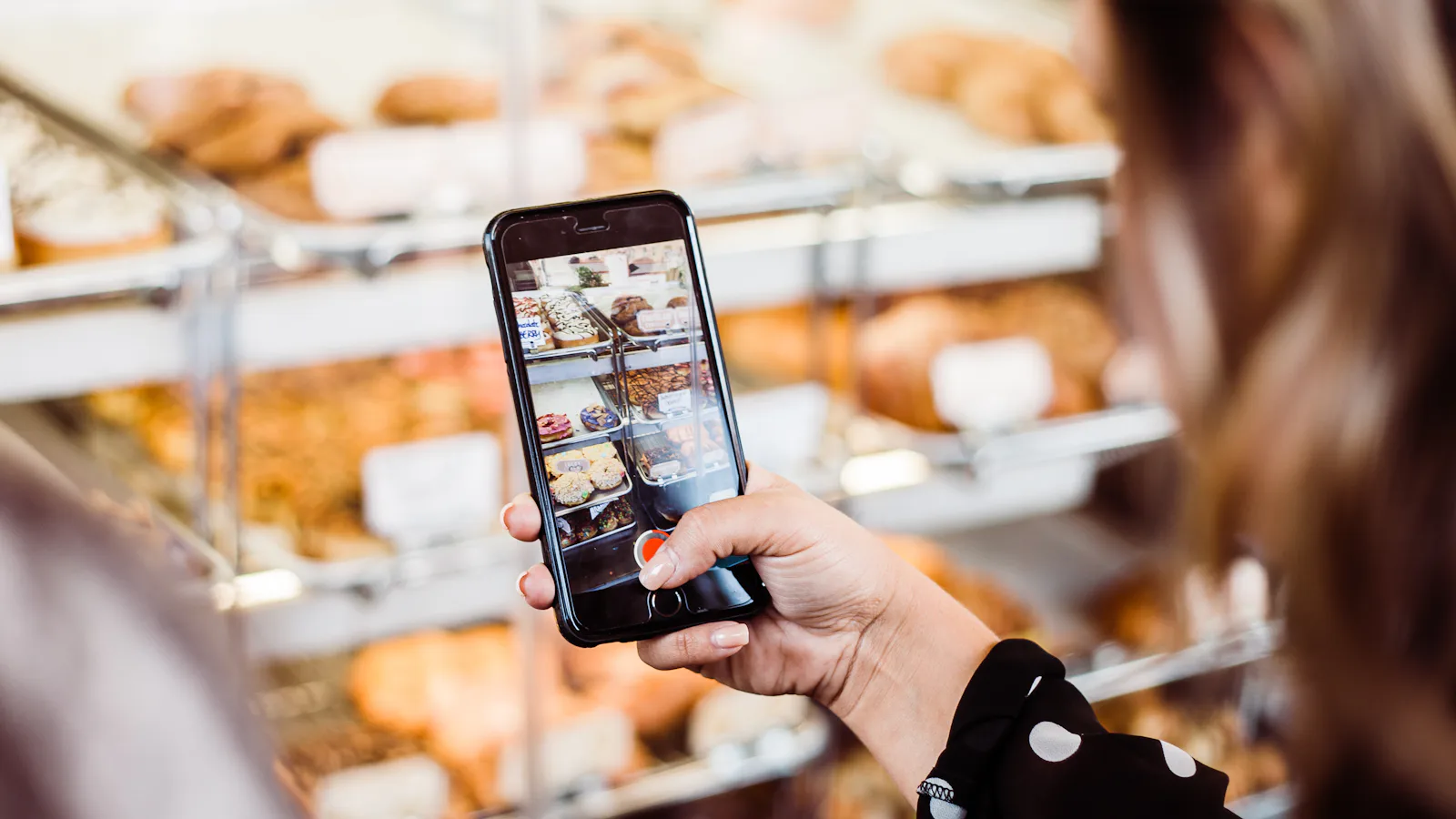 Femme qui photographie une vitrine de pâtisseries avec son iPhone