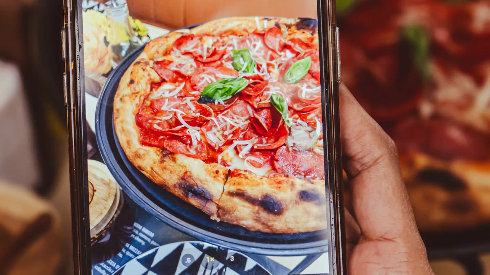 Cliente qui photographie sa pizza au téléphone dans une pizzeria